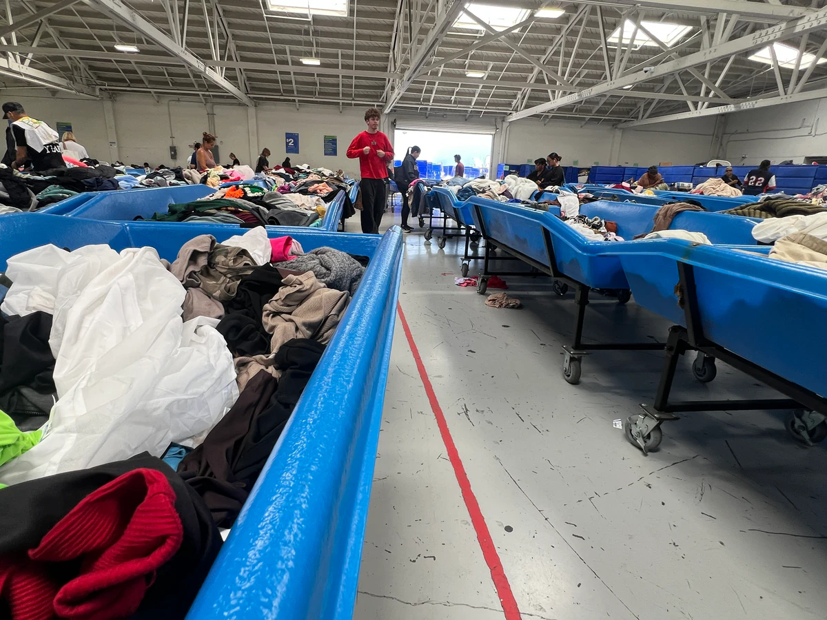 Goodwill Auction & Outlet Store in Long Beach, California, featuring shoppers searching through bulk textile containers.